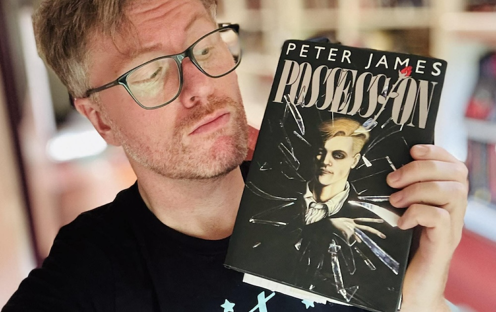 Aaron Dries holds up a copy of Peter James's book Possession, with something mysterious that looks a bit like a letter poking out the bottom.